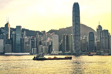 Dry cargo vessel at Victoria Harbor of Hong Kong at sunset. View from Kowloon on HK Island.