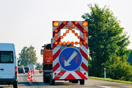 Truck carrying arrow down left reflective direction road sign in highway in Poland.