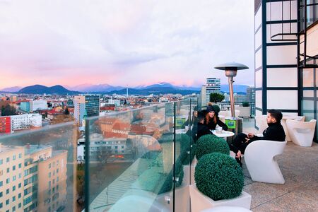 Ljubljana, Slovenia - January 14, 2019: Couple at street cafe terrace with tables and chairs and beautiful panoramic view in Ljubljana old city, sunset, Slovenia. People at Modern restaurant verandaのeditorial素材