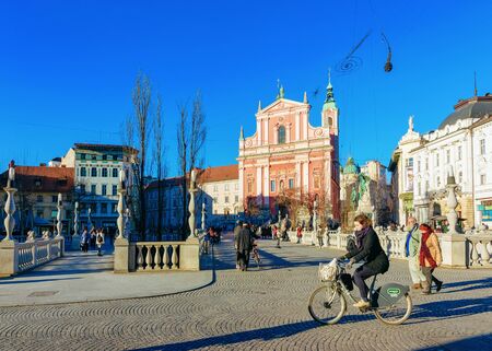 Ljubljana, Slovenia - January 14, 2019: Woman on bicycle at Franciscan Church and Triple Bridge over Ljubljanica River in Ljubljana old town streets, Slovenia. Cathedral towers and Slovenian cityのeditorial素材