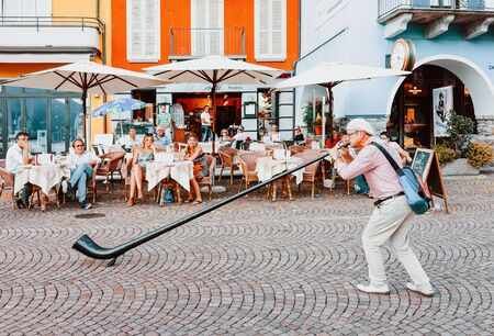 Ascona, Switzerland - August 23, 2016: Alphorn player at street cafe in romantic luxury resort in Ascona town on Lake Maggiore in Ticino canton in Switzerland. Outdoor expensive family restaurantsのeditorial素材