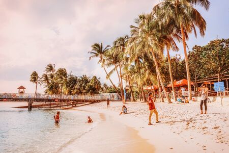 Singapore, Singapore - March 1, 2016: Couple taking photos at the sea on Siloso Beach at Sentosa island resort in Singapore. It is artificial beach with a sand taken from Malaysia and Indonesia. Tonedのeditorial素材