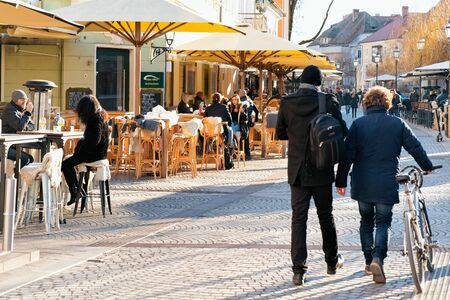 Ljubljana, Slovenia - January 15, 2019: Tourists with bicycle and Tourists eat and drinking in restaurants, tables and chairs in Ljubljana old town embankment, Slovenia. People in open air city cafesのeditorial素材