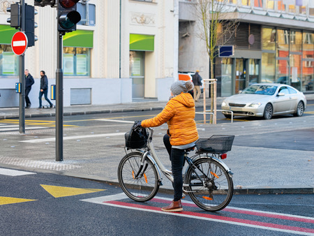 Woman riding bicycle and crossing road street of Ljubljana old town, Slovenia. People on bike and cycle in Slovenian city view in winter. Cyclist and road landmark. Urban green capital.の写真素材