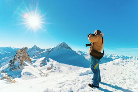 Man with digital camera taking photos in Hintertux Glacier ski resort in Zillertal in Tyrol in Austria in winter in Alps. Alpine mountains with snow. Person and Blue sky and white slopes.の写真素材
