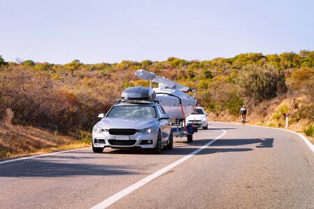 Car with yacht or motor boat at the road in Sardinia island in Italy in summer. Auto with motorboat on the highway in Europe. View on moped on motorway.の写真素材