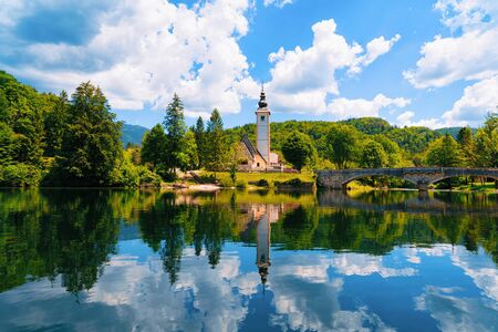 Scenery and Church of St John Baptist on Bohinj Lake at Slovenia. Nature in Slovenija. View of blue sky with clouds. Beautiful landscape in summer. Alpine Travel destination. Julian Alps mountainsの写真素材