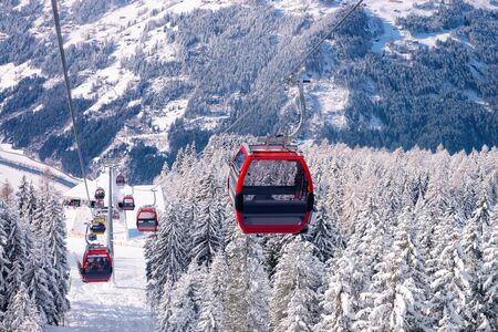 Red Cable cars of Zillertal Arena ski resort in Tyrol in Mayrhofen in Austria in winter Alps. Chair lifts in Alpine mountains with white snow and blue sky. Downhill fun at Austrian snowy slopes.の写真素材