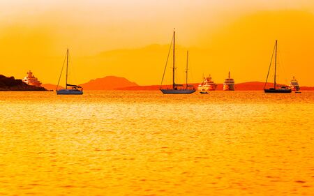 Sunrise or sunset with yachts at Porto Rotondo at the Mediterranean sea in Sardinia island of Italy. Boat in Sardegna in summer. Landscape of Olbia province. Mixed media.の写真素材