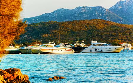 Sunrise or sunset with yachts at Porto Rotondo on Costa Smeralda at Mediterranean sea in Sardinia island of Italy. Boat in Sardegna in summer. Landscape of Olbia province. Mixed media.の写真素材