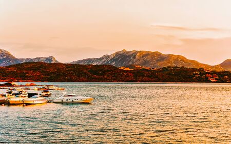 Sunrise or sunset with yachts at Porto Rotondo on Costa Smeralda at Mediterranean sea in Sardinia island of Italy. Boat in Sardegna in summer. Landscape of Olbia province. Mixed media.の写真素材