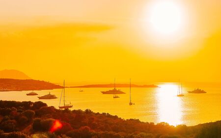Sunrise or sunset with yachts at Porto Rotondo at the Mediterranean sea in Sardinia island of Italy. Boat in Sardegna in summer. Landscape of Olbia province. Mixed media.の写真素材