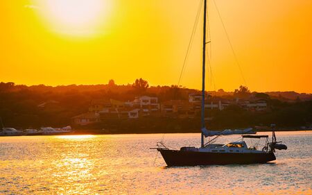 Sunrise or sunset with yachts at Porto Rotondo on Costa Smeralda at Mediterranean sea in Sardinia island of Italy. Boat in Sardegna in summer. Landscape of Olbia province. Mixed media.の写真素材