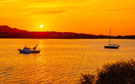 Sunrise or sunset with yachts at Porto Rotondo at the Mediterranean sea in Sardinia island of Italy. Boat in Sardegna in summer. Landscape of Olbia province. Mixed media.の写真素材