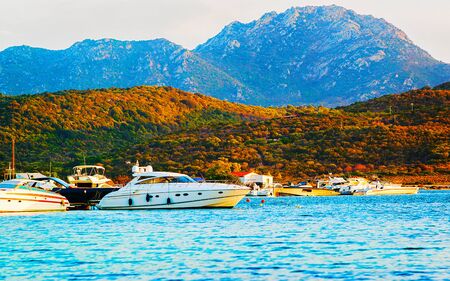 Sunrise or sunset with yachts at Porto Rotondo on Costa Smeralda at Mediterranean sea in Sardinia island of Italy. Boat in Sardegna in summer. Landscape of Olbia province. Mixed media.の写真素材