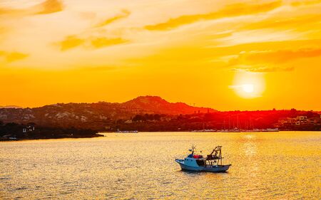 Sunrise or sunset with yachts at Porto Rotondo on Costa Smeralda at Mediterranean sea in Sardinia island of Italy. Boat in Sardegna in summer. Landscape of Olbia province. Mixed media.の写真素材