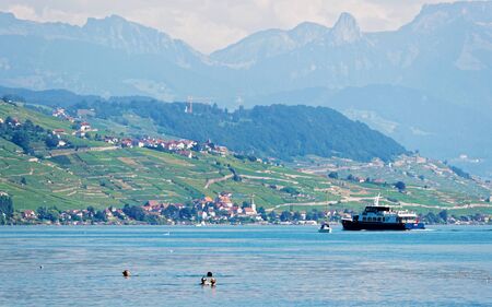 Lausanne, Switzerland - August 26, 2016: People swimming and water ferry on Lake Geneva at Ouchy embankment in Lausanne, Switzerland. People aboard. Mixed media.のeditorial素材