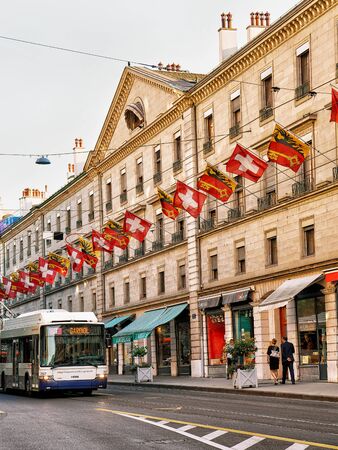 Geneva, Switzerland - August 30, 2016: Tram on Rue de la Corraterie Street with Swiss flags in the center of Geneva, Switzerland. People on the background. Mixed media.のeditorial素材