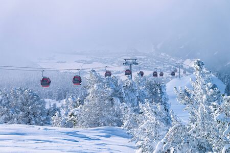 Red Cable cars among clouds in Zillertal Arena ski resort in Tyrol in Mayrhofen in Austria in winter Alps. Chair lifts in Alpine mountains with white snow and blue sky. Downhill fun at snowy slopes.の写真素材
