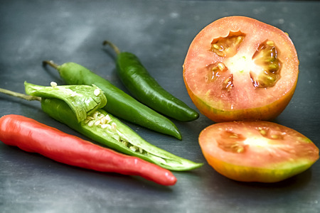 One red chilly and three green chilly with one cleaved plus cut tomatoの写真素材