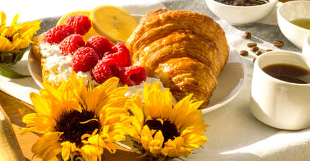 croissants with raspberries and whipped cream on a tray with coffee and sunflowersの写真素材