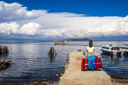 Cholita, native woman of the bolivian Andes, in a deck with red bags and totora boat in lake Titicaca, Bolivia.のeditorial素材