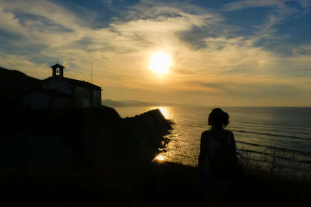 Sunset in the coast with church and woman silhouette. Basque Country coast in North of Spainの写真素材