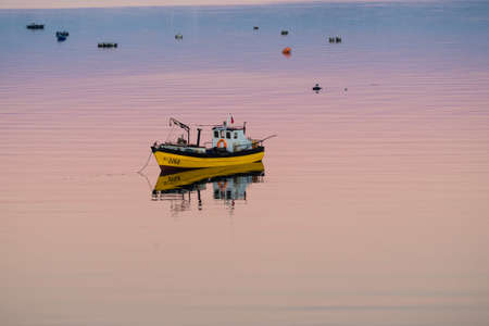 Little boat floating on the calm water under amazing sunset in Quellon, Chiloe Island in Chileのeditorial素材