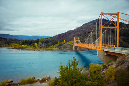 Red suspension bridge over the water runoff of General Carrera Lake, near Lake Bertrand, Puerto Tranquilo, Chile Chico, Aysen, Chileの写真素材