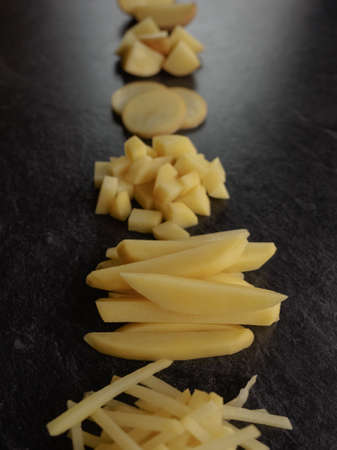Different cuts of potatoes on a black textured background. Photo taken from above