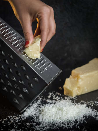 Hand of a woman grating parmesan cheese on a black background. Dark food. Italian cheese Parmigiano Reggianoの写真素材