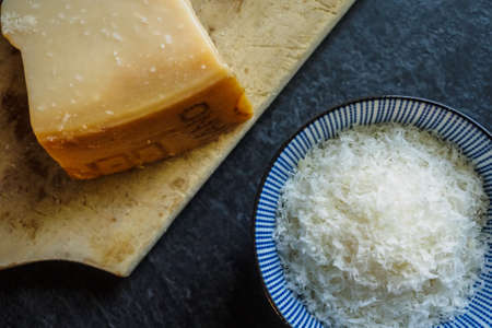 Grated parmesan cheese in a bowl on black background, italian food. Dark food