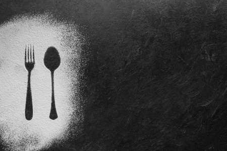 Spoon and fork silhouette made with flour on dark texture background, up horizontal viewの写真素材