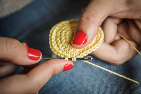 Girl doing crochet with yellow yarn and nails painted red, close up photography
