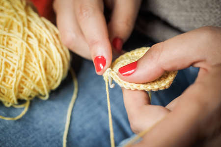Girl doing crochet with yellow yarn and nails painted red, close up photographyの写真素材