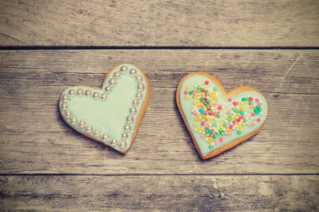 Two baked hearts covered with blue icing. Wooden background, from above.