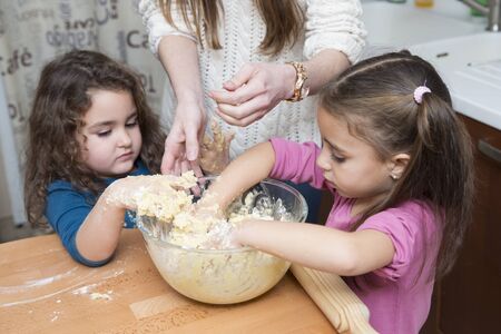 Two lovely girls and mother mixing dough with hands