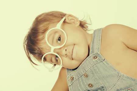 Portrait of smiling little girl wearing denim overall and white glasses looking at cameraの写真素材