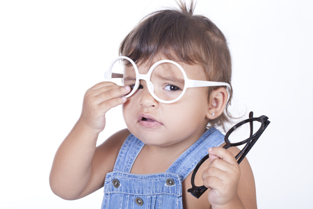 Sad little girl trying on pair of white glasses while holding black ones.Isolatedの写真素材