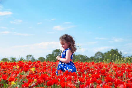Side view of cute lovely girl in blue dress standing in bright red blossoming fieldの写真素材