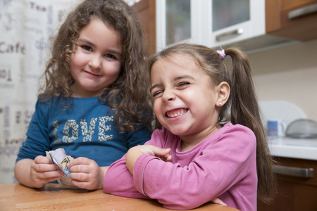 Two cute kids smiling and making faces at camera in kitchenの写真素材