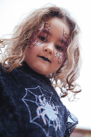 Little girl with spider web painted on face looking at camera. Halloweenの写真素材
