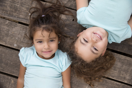 Top view of two pretty girls with curly hair looking at camera with smile over wooden background.の写真素材