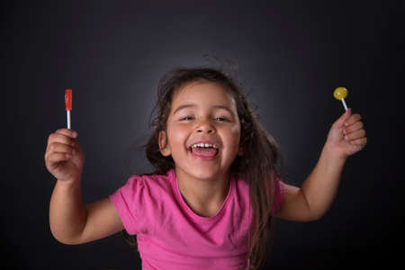 Portrait of a caucasian four years girl laughing with some candies. Black background. Studio shotの写真素材