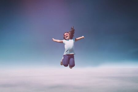 Small girl jumping on blue sky and cloudsの写真素材
