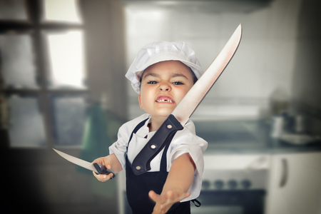 Funny portrait of a six years girl dressed as a cook throwing a knifeの写真素材