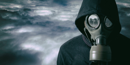 Portrait of a man with a gas mask in a dramatic of cloudy background. There is a contaminant factory in the reflection of the glassesの写真素材