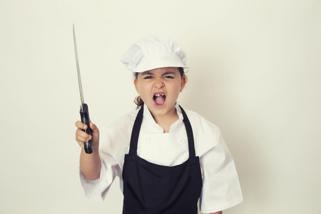 Little chef girl screaming with a knife in the handの写真素材