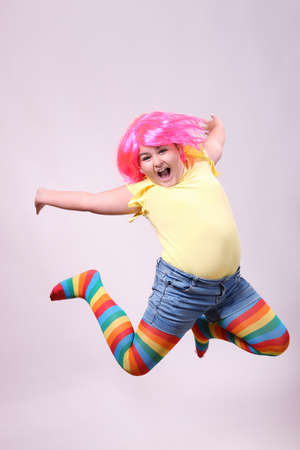 Nine years old girl with a pink wig jumping and screaming on a white background