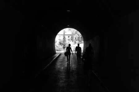 Group of 3 people walking through a tunnel while a boy plays the guitar and another girl practices running. They cross the tunnel that passes under the Gibralfaro Castle in the city of Malaga, Andalucia. Photograph taken on April 30 at the holidays of May 1, Labor Day.の写真素材